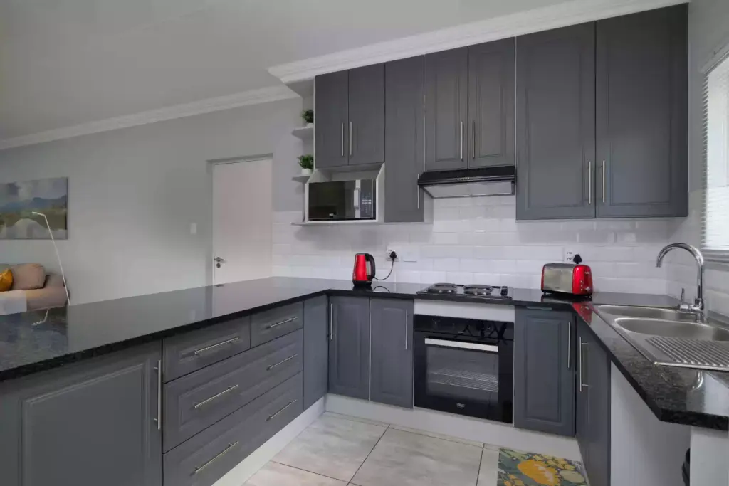 Wide view of modern kitchen with dark charcoal shaker cabinets, white marble waterfall island and marble tile floor